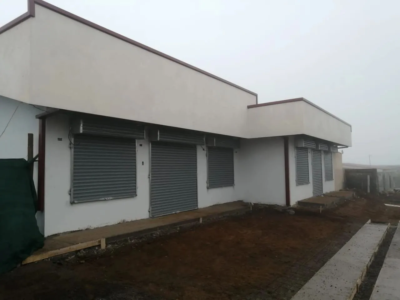 Edificio de una planta con seis cortinas metálicas grises cerradas.